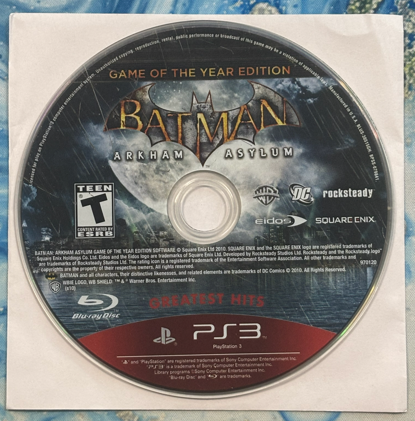 Batman Arkham Asylum Game of the Year Edition disc on a blue and white patterned background