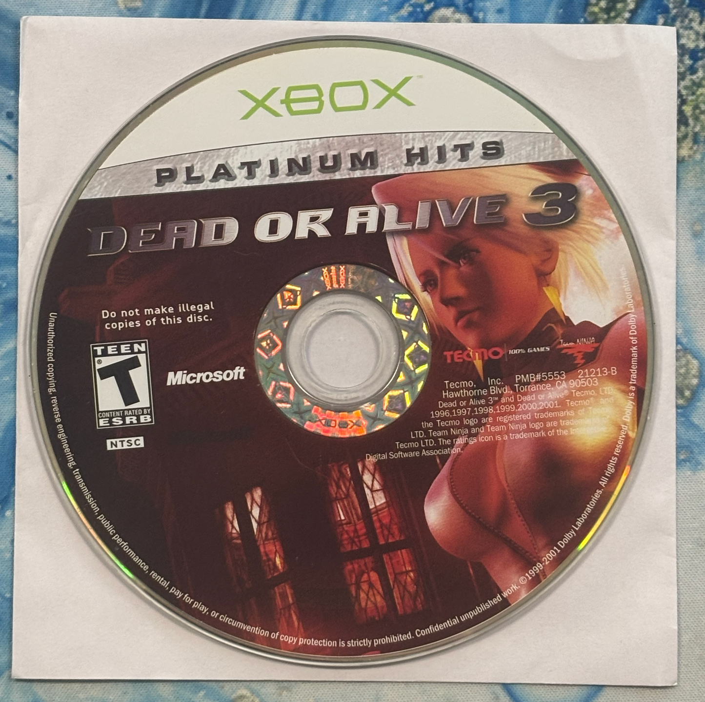 Xbox Platinum Hits 'Dead or Alive 3' game disc with Xbox logo on a textured surface