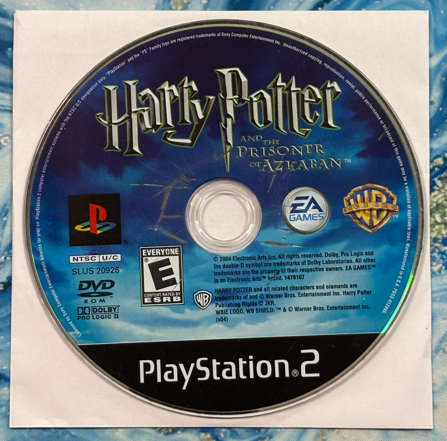 PlayStation 2 game disc for 'Harry Potter and the Prisoner of Azkaban' on a textured blue and white background.