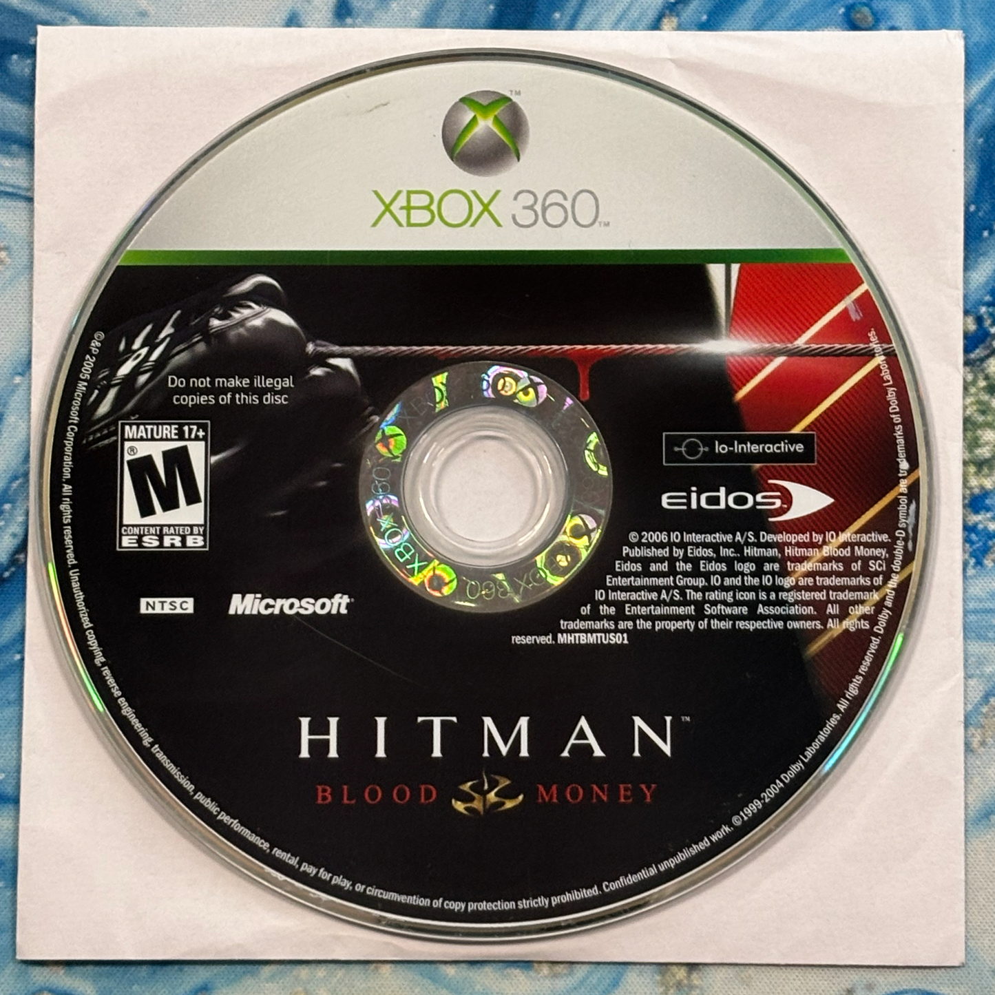 Xbox 360 game disc for 'Hitman: Blood Money' on a textured surface