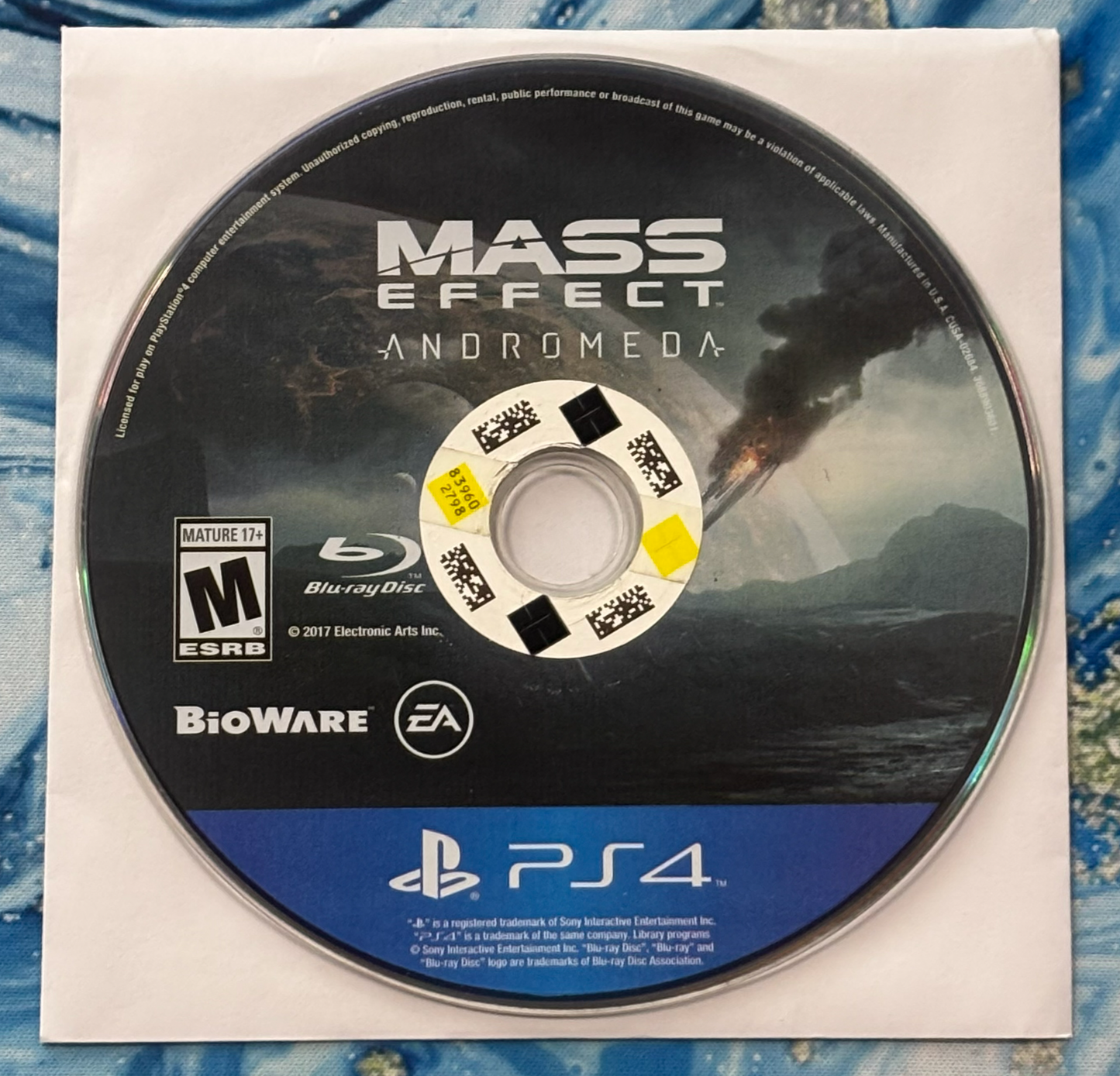 Mass Effect Andromeda game disc for PlayStation 4 on a textured surface