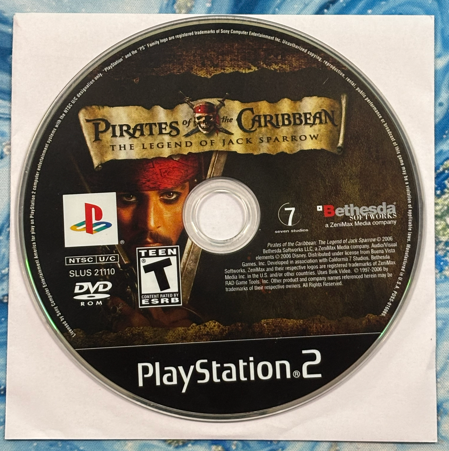 PlayStation 2 game disc for 'Pirates of the Caribbean: The Legend of Jack Sparrow' on a textured surface.