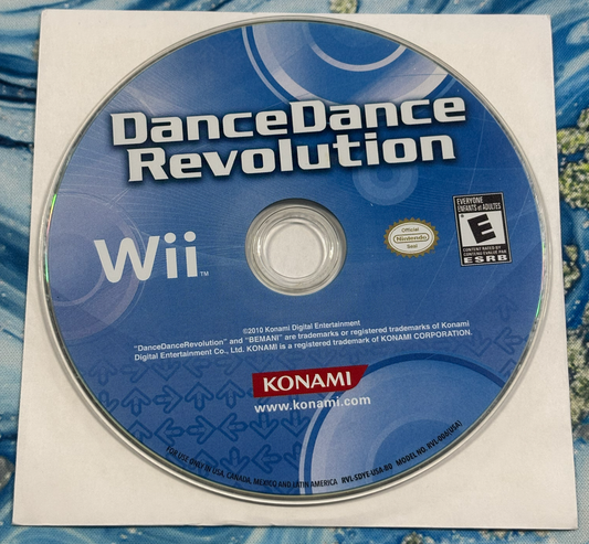 A used Nintendo Wii game disc for DanceDance Revolution, still in its original white paper sleeve, photographed flat on a blue patterned fabric background.