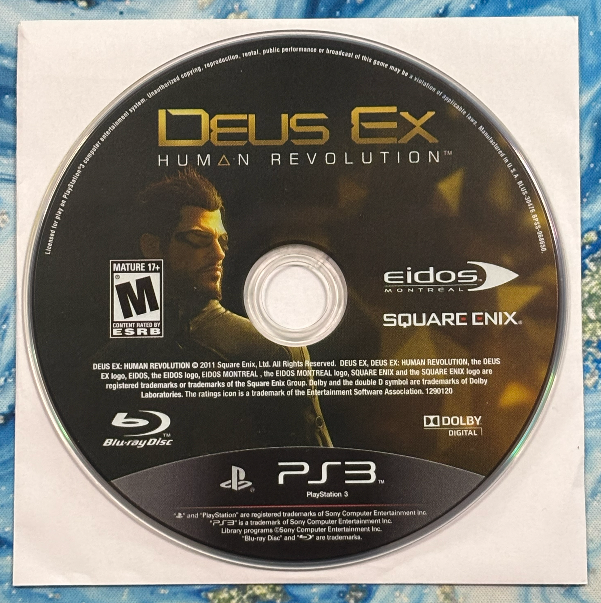Deus Ex: Human Revolution PlayStation 3 game disc on a textured surface