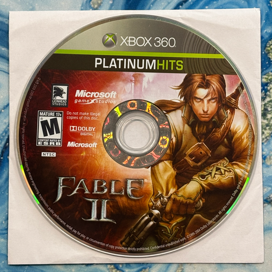 Xbox 360 Platinum Hits disc for 'Fable II' game on a textured blue surface