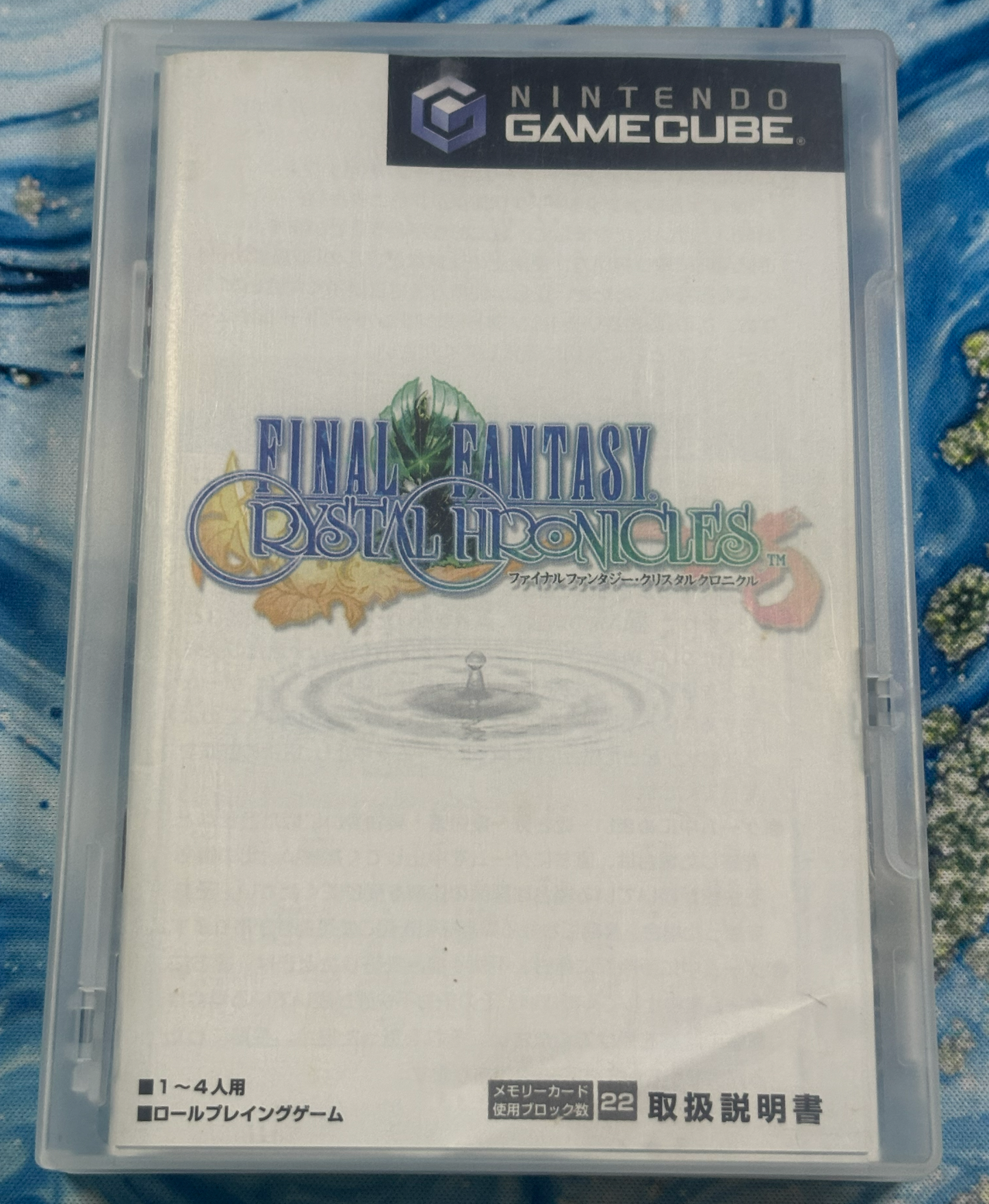 Nintendo GameCube game case for Final Fantasy Crystal Chronicles, showing the front cover art in a clear plastic case against a blue patterned background.