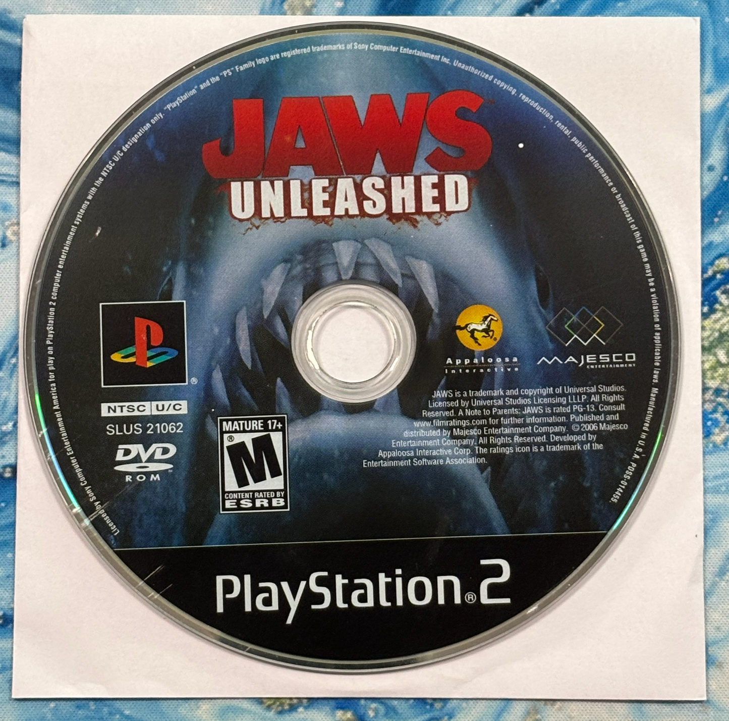 PlayStation 2 game disc for 'Jaws Unleashed' on a textured blue and white background