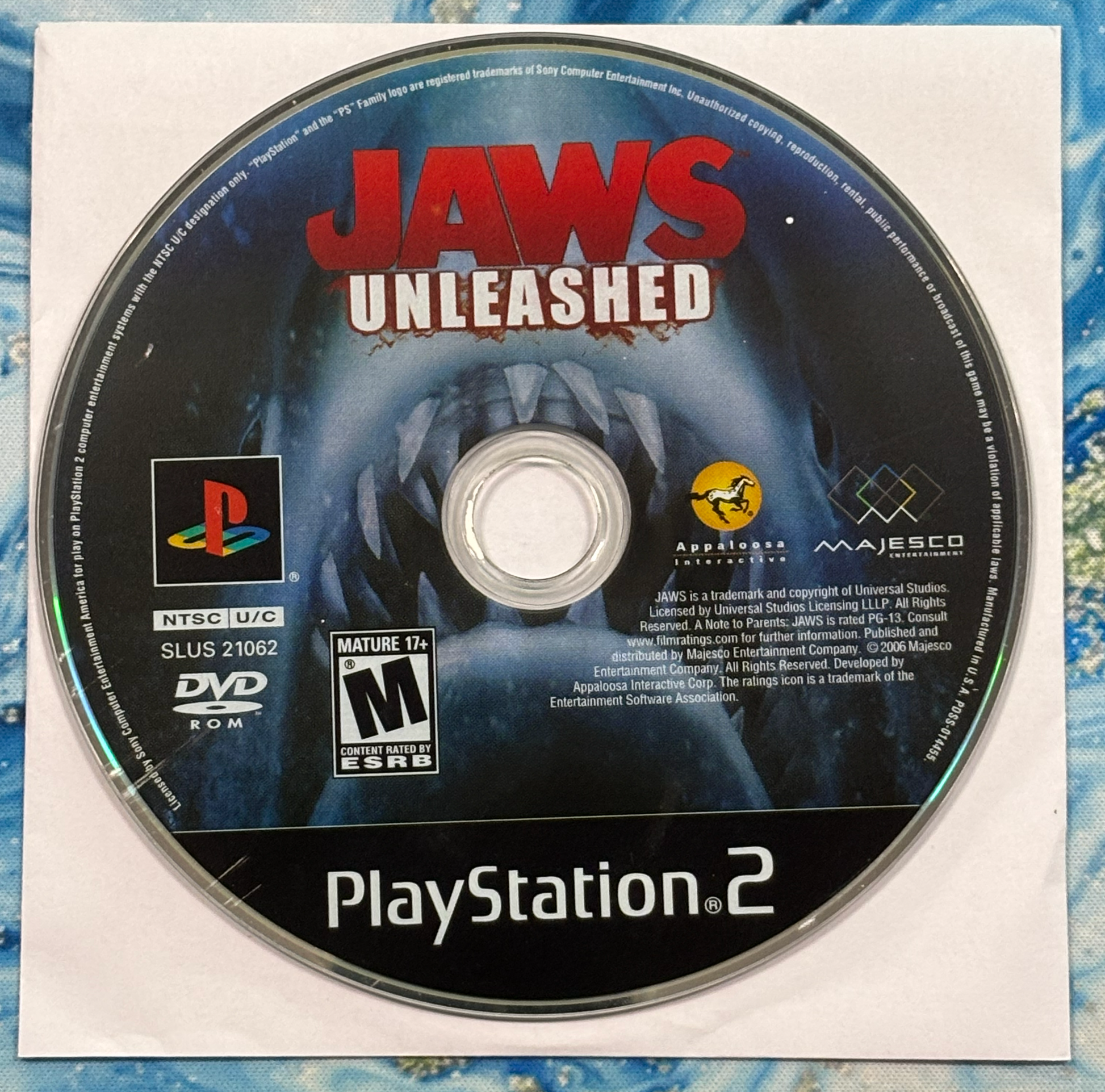 PlayStation 2 game disc for 'Jaws Unleashed' on a textured blue and white background