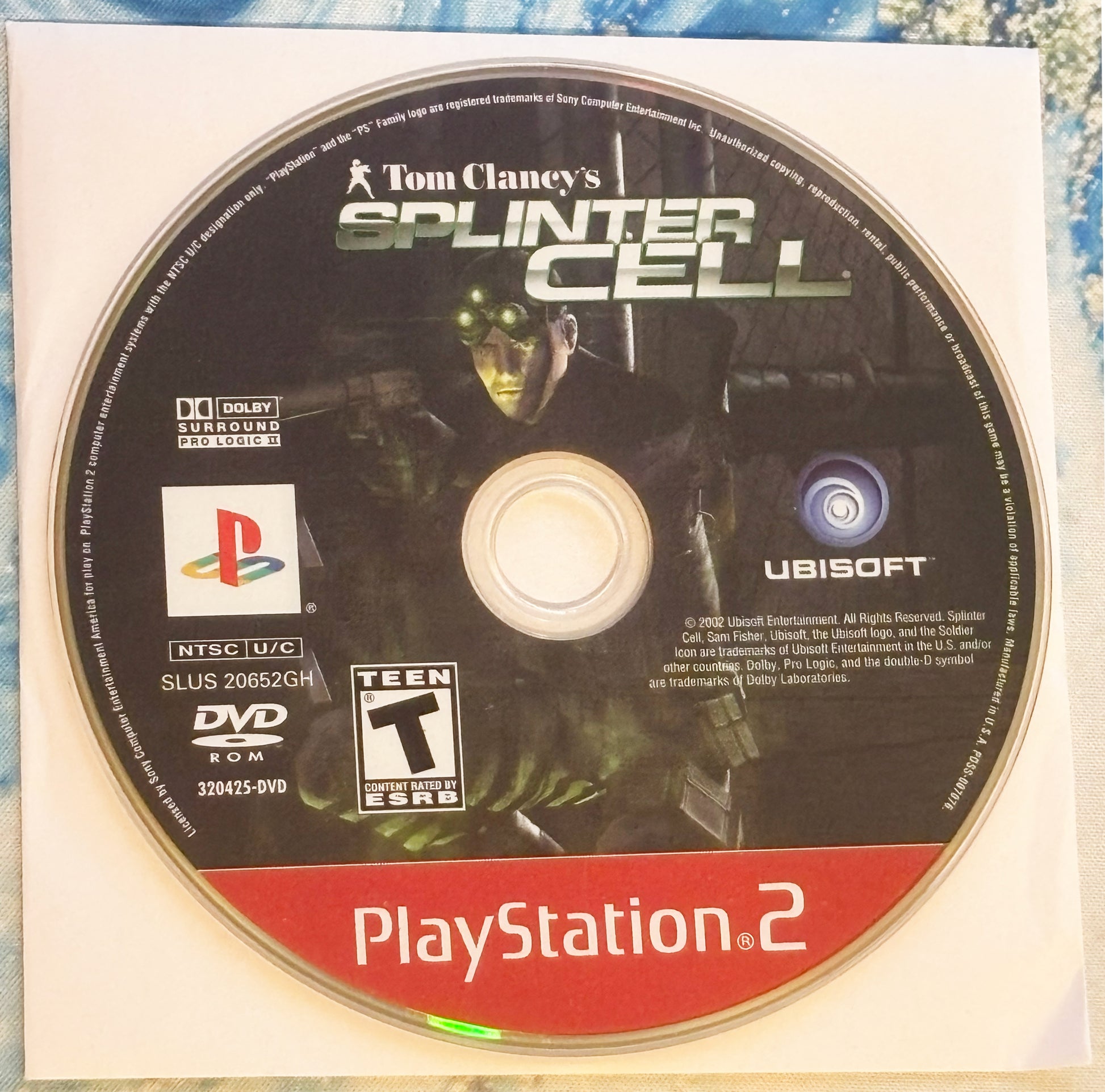 Tom Clancy's Splinter Cell PlayStation 2 game disc on a textured surface